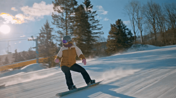 A snowboarder carves down a sunlit groomed run at Camelback Resort, spray lifting behind the board.